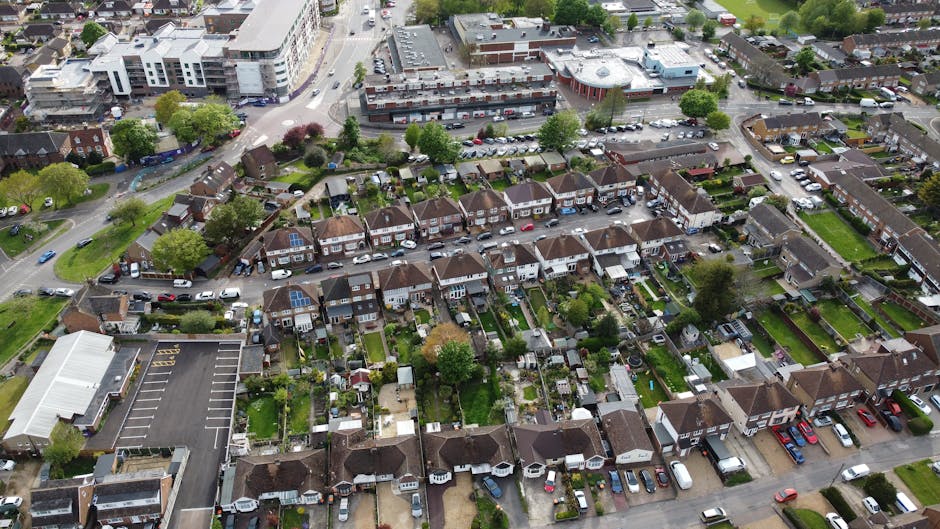 An aerial view of a residential neighborhood showing multiple rows of terraced houses with small front and back gardens, well-maintained lawns, and paved patios. The gardens feature a variety of plant